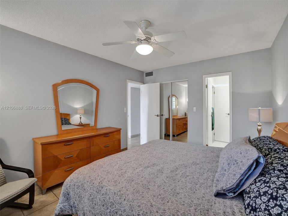 Spacious room featuring neutral paint tones, ceramic tile flooring, a white ceiling fan with integrated lighting, and a dual-panel sliding closet with mirrored doors