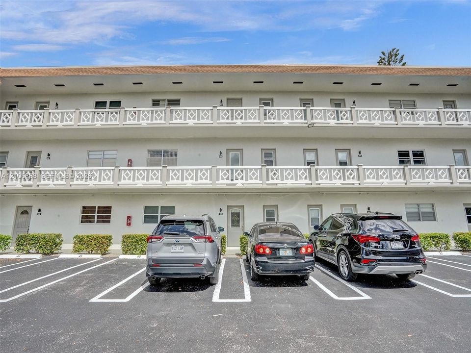Multi-story building exterior featuring white stucco facade, decorative lattice railings, and private balconies with individual entries