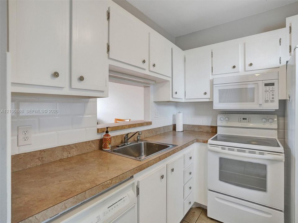 Kitchen featuring white cabinetry, solid-surface countertops, white subway tile backsplash, stainless steel undermount sink, and white appliances