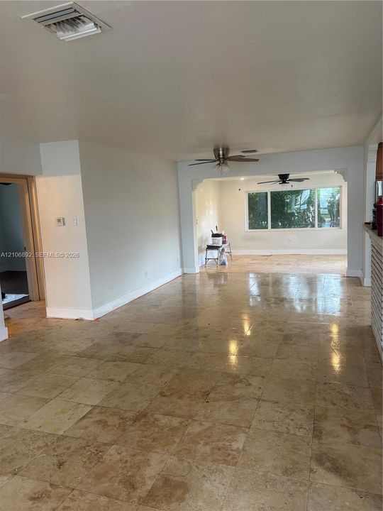 Large-format neutral stone flooring, dual ceiling fans, expansive windows, and arched architectural detailing