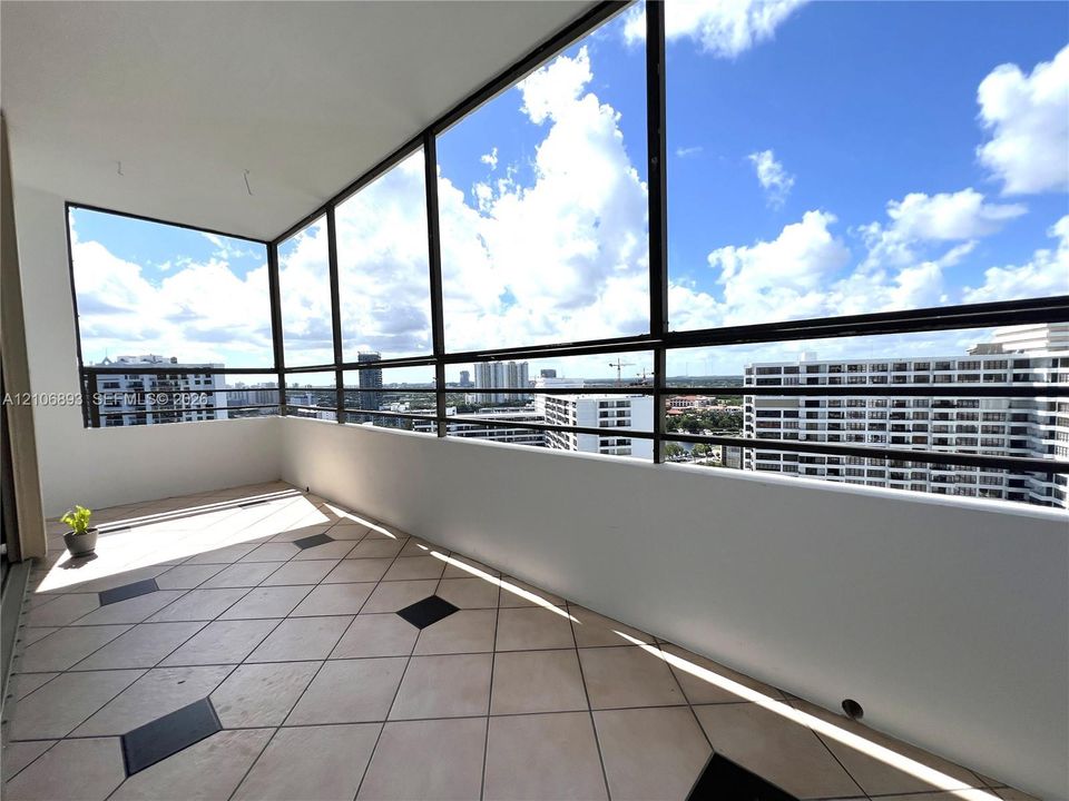 Enclosed balcony featuring floor-to-ceiling metal-framed windows, diamond-pattern tile flooring with dark accent inlays, and solid wall surrounds