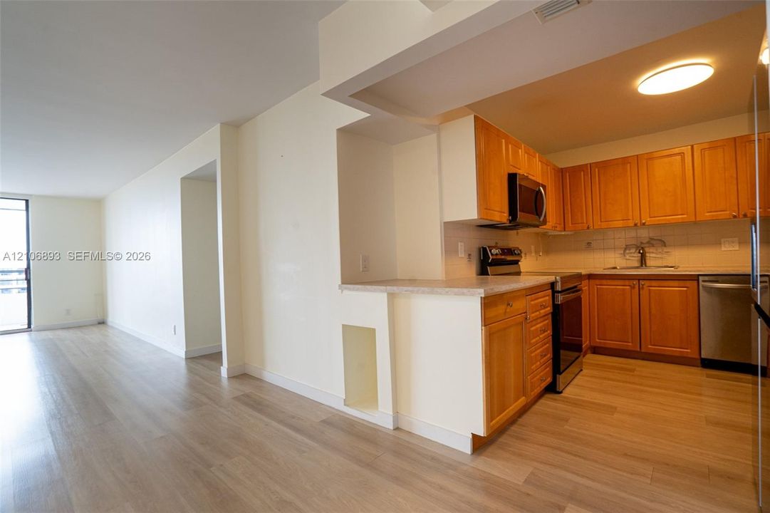 Kitchen featuring wood cabinetry, stainless steel appliances, neutral stone-finish countertops, and wood-finish flooring