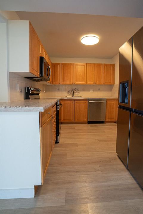 Kitchen featuring wood cabinetry, stone-finish countertops, stainless steel appliances, and wood-finish flooring