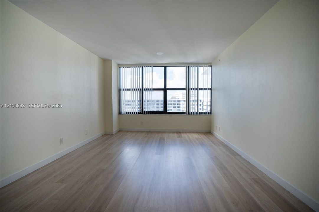 Interior room featuring wood-finish flooring, neutral wall tones, and expansive floor-to-ceiling windows with vertical blinds