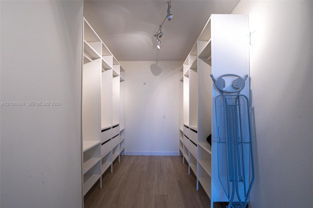 Custom walk-in closet featuring extensive built-in cabinetry, multiple hanging sections, integrated shelving, pull-out drawers, and track lighting over wood-finish flooring