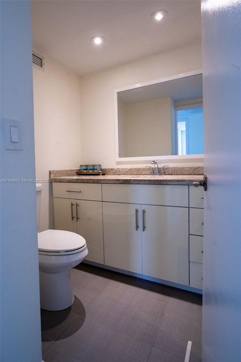 Bathroom featuring a white cabinetry vanity, stone-finish countertop with an integrated basin, large rectangular wall-mounted mirror, and tile flooring