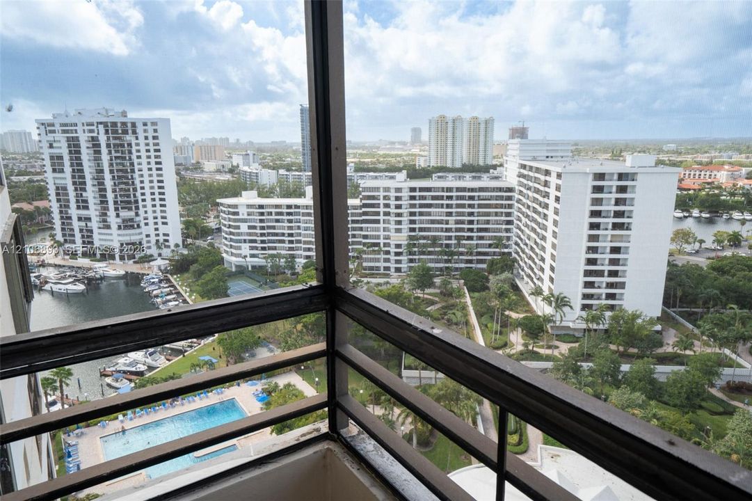 Enclosed balcony featuring metal railing and panoramic exterior perspective of the marina, swimming pool, and surrounding urban landscape