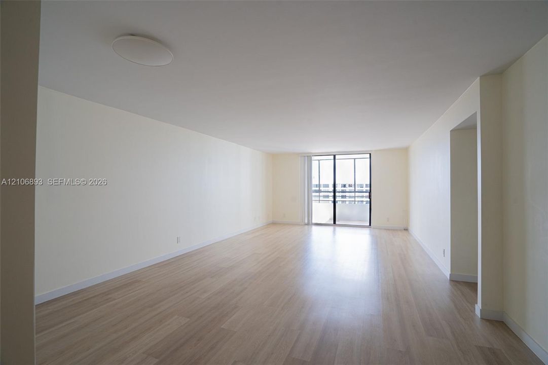 Open interior featuring light-tone wood-finish flooring, smooth ceilings, and sliding glass door access to a balcony