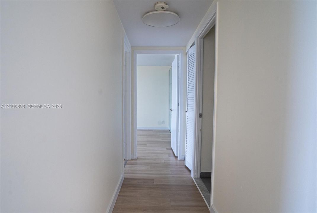 Hallway featuring wood-finish flooring, white door casings, and a white louvered closet door