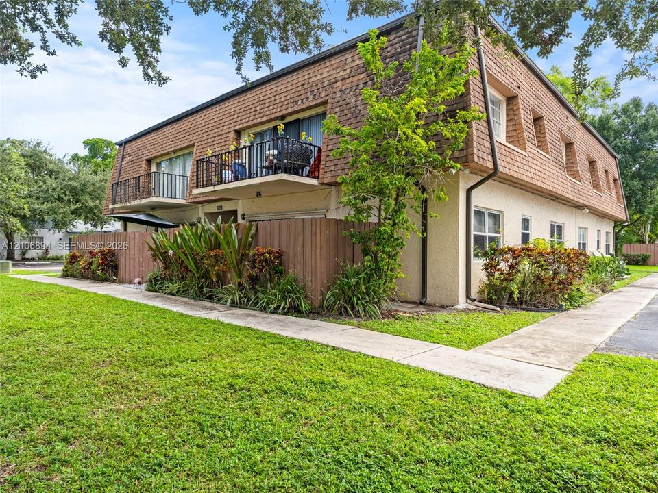 Two-story exterior featuring textured stucco siding, cedar shake mansard roofline, metal balcony railings, and wood privacy fencing