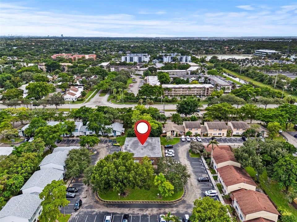 Aerial perspective featuring established landscaping, mature trees, designated parking areas, and flat roofing construction