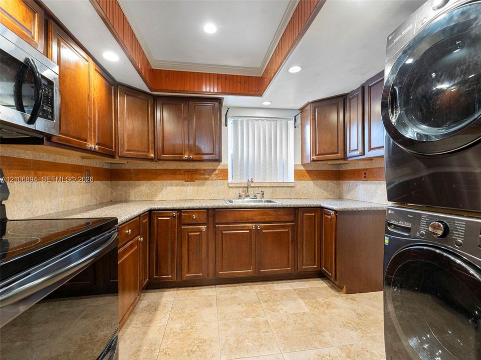 Wood cabinetry with recessed panels, stone-finish countertops, tiled flooring, integrated laundry units, and recessed ceiling lighting