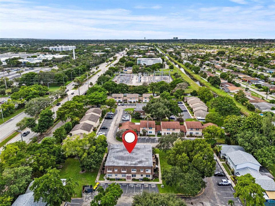 Aerial perspective of a multi-unit residential building featuring a flat roofline, brick facade, dedicated surface parking, and mature landscape surroundings