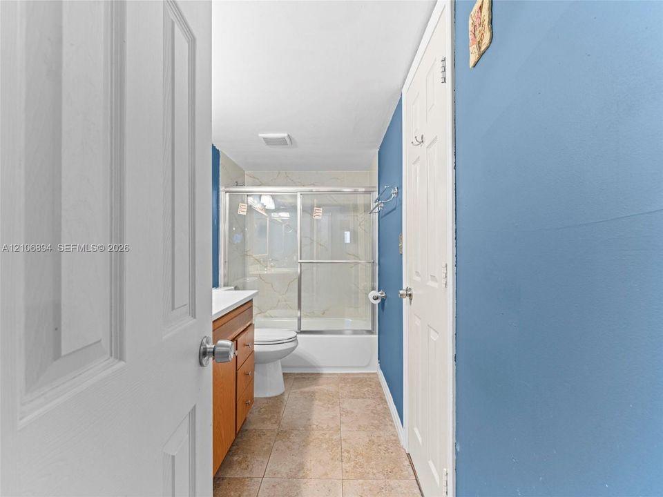 Bathroom featuring ceramic tile flooring, a wood-finish vanity cabinet, a tub-shower combination with a sliding glass door enclosure, and a built-in towel rack
