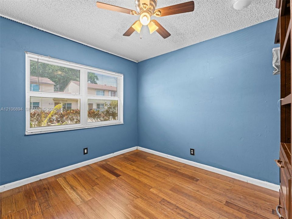 Room featuring wood-finish flooring, a multi-pane window with integrated blinds, and a ceiling-mounted light fixture with a fan