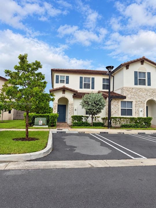 Two-story stucco and stone veneer exterior featuring a tile roof, arched entryway, shuttered windows, and dedicated reserved parking