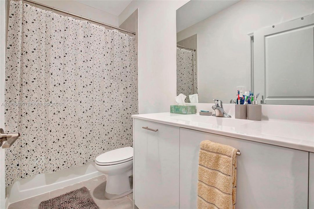 White vanity with an integrated countertop, polished chrome faucet, expansive wall-mounted mirror, and a porcelain toilet