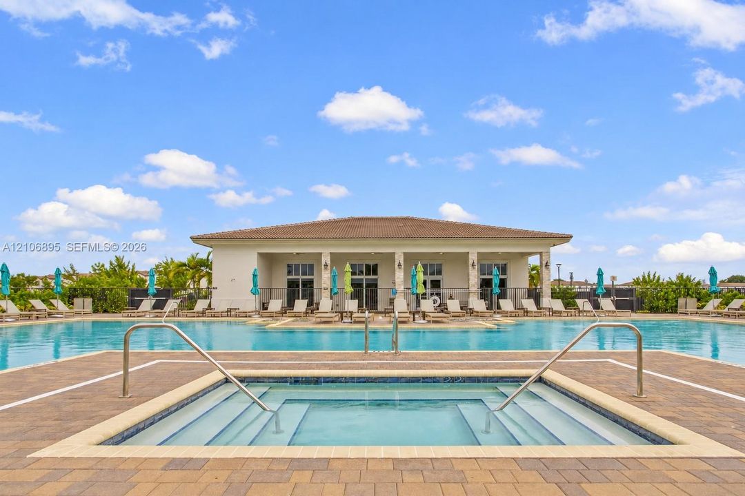 In-ground swimming pool and spa featuring paver decking, tiled borders, and metal handrails