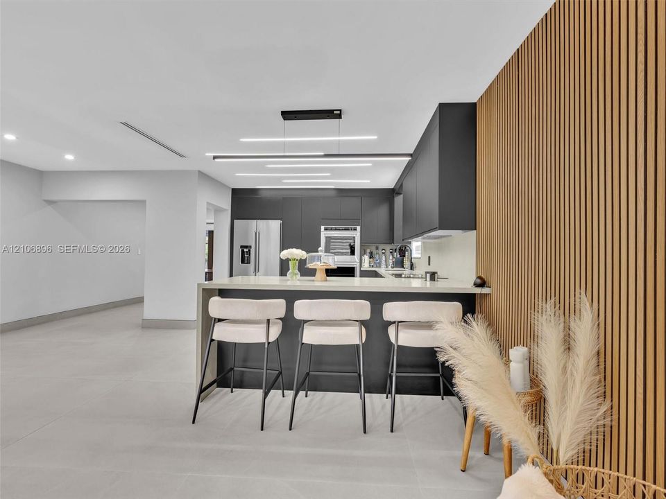 Kitchen featuring matte dark cabinetry, a waterfall-edge island with stone-finish countertop, linear LED pendant lighting, and a floor-to-ceiling wood slat accent wall