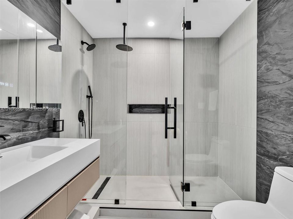 Bathroom featuring a floating vanity with integrated sink, walk-in shower with frameless glass enclosure, dual shower heads including a ceiling-mounted rainfall fixture, and recessed wall niche
