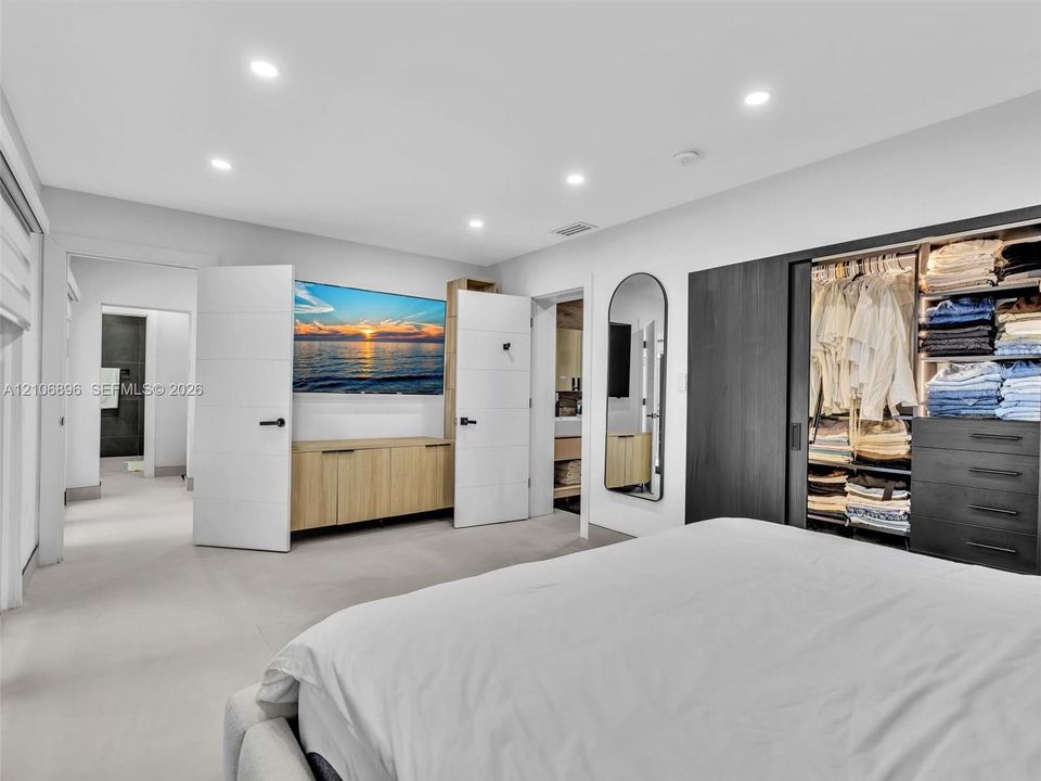 Recessed lighting, built-in light-wood cabinetry, dark wood-finish sliding closet doors with integrated shelving and drawer storage, and wall-mounted arched mirror