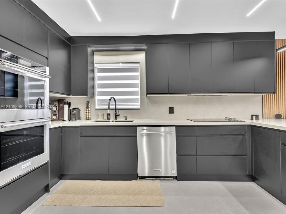 Modern kitchen featuring matte charcoal cabinetry, stainless steel double wall ovens and dishwasher, light-toned solid surface countertops, and linear recessed ceiling lighting