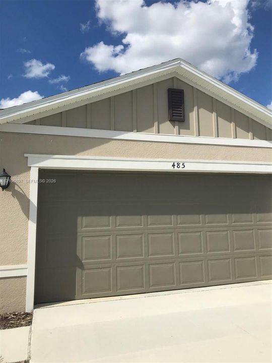 Garage exterior featuring a paneled sectional door, board-and-batten siding, a gable roofline with decorative louver, and an attached exterior wall-mounted lantern