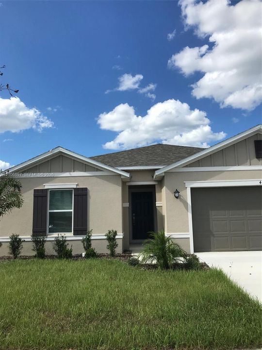 Single-story exterior featuring a neutral stucco facade, decorative shutters, concrete driveway, and attached garage