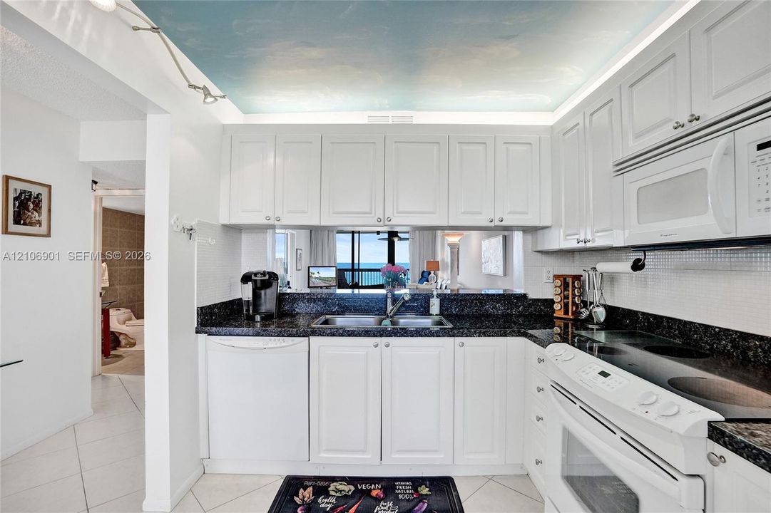 Kitchen featuring white cabinetry, dark stone countertops, built-in white appliances, and a ceiling mural