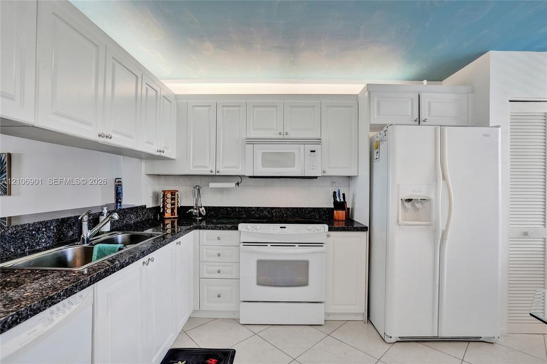Kitchen featuring white cabinetry, dark stone-finish countertops, tile flooring, and integrated white appliances