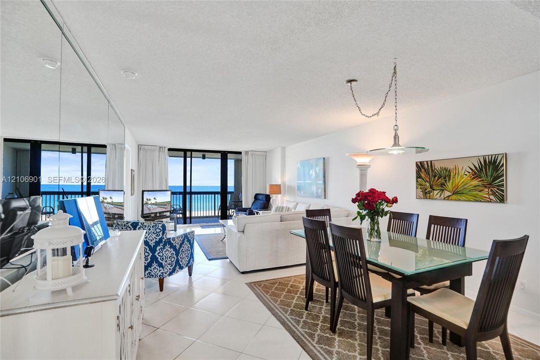 Open-concept area featuring light-toned tile flooring, floor-to-ceiling mirror wall paneling, sliding glass doors, and a suspended metal pendant light fixture