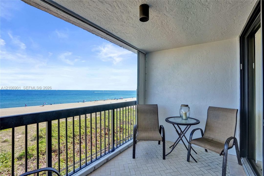 Covered balcony featuring herringbone-patterned tile flooring, black metal railing, and direct water and beach frontage