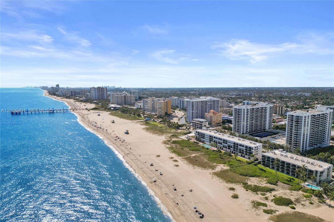 Coastal aerial perspective featuring expansive sandy shoreline, turquoise ocean waters, and regional cityscape
