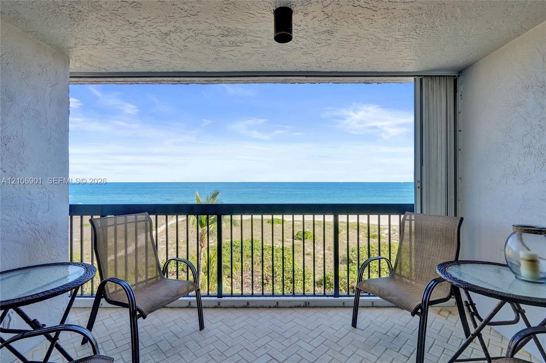 Covered balcony featuring herringbone-patterned tile flooring, textured stucco walls, black metal railing, and ocean horizon backdrop