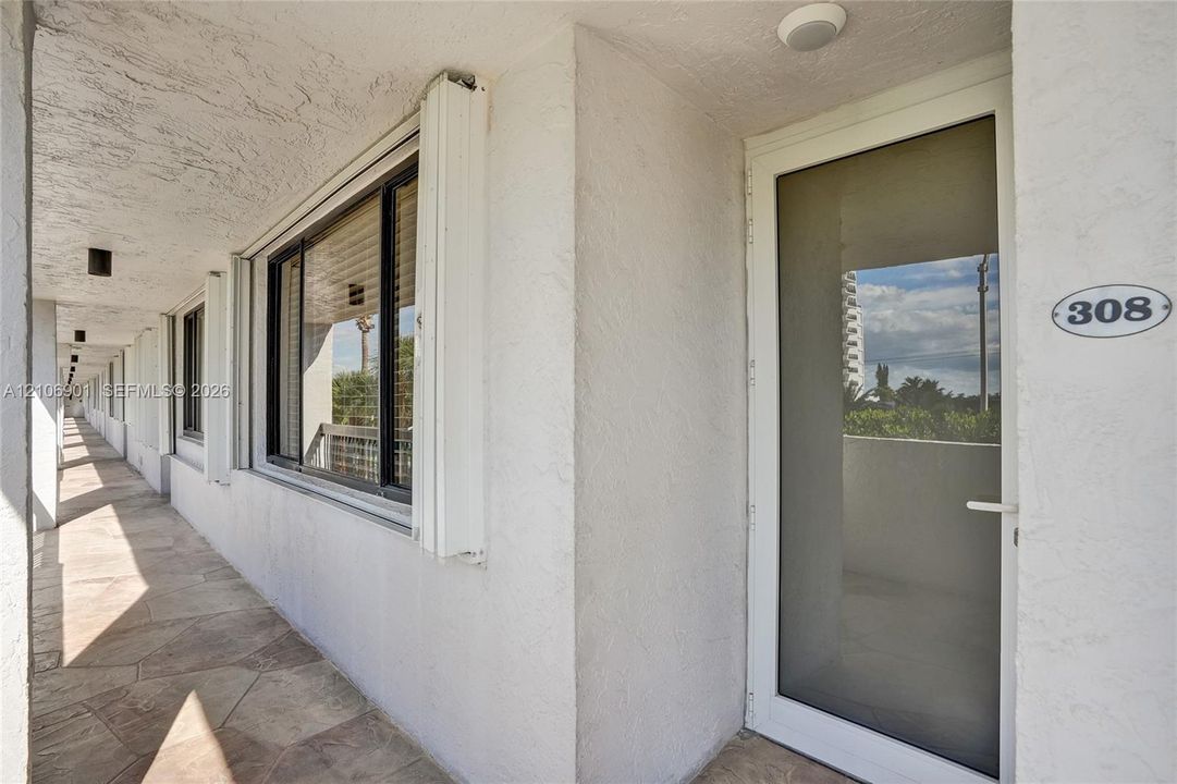 Exterior entry featuring a full-length glass storm door, textured white stucco walls, stone-finish tile flooring, and flush-mount exterior lighting