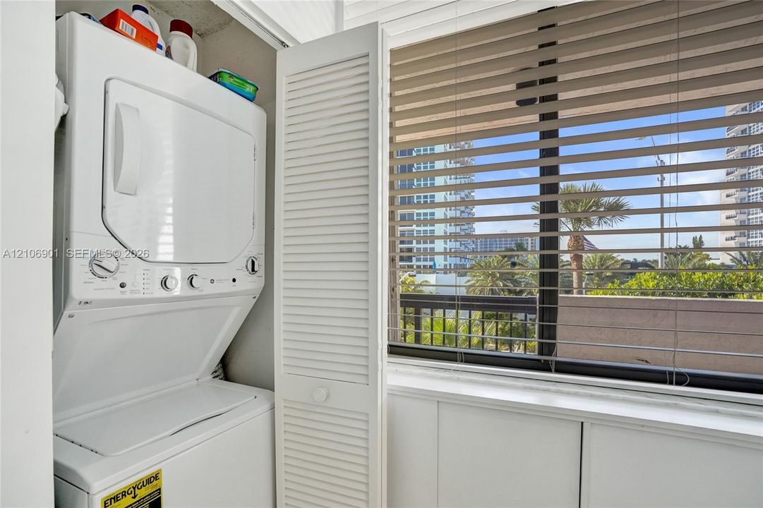 Stacked laundry unit featuring louvered bi-fold doors and large window with horizontal blinds