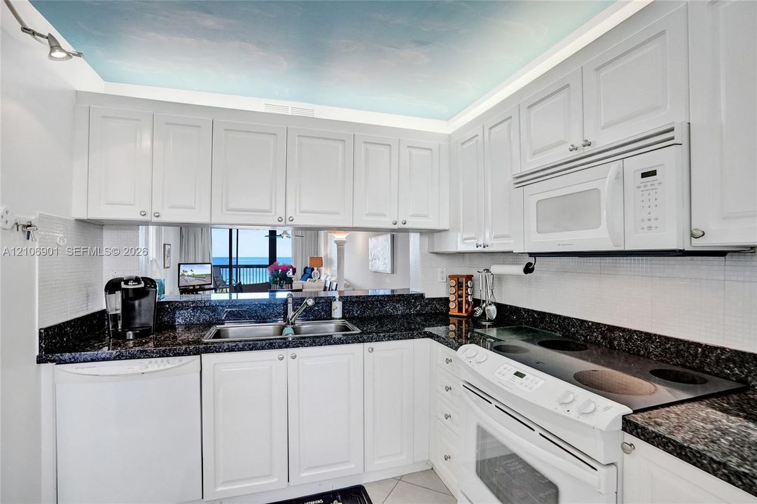 Kitchen featuring white cabinetry, dark stone countertops, built-in microwave, integrated electric cooktop, and tile backsplash