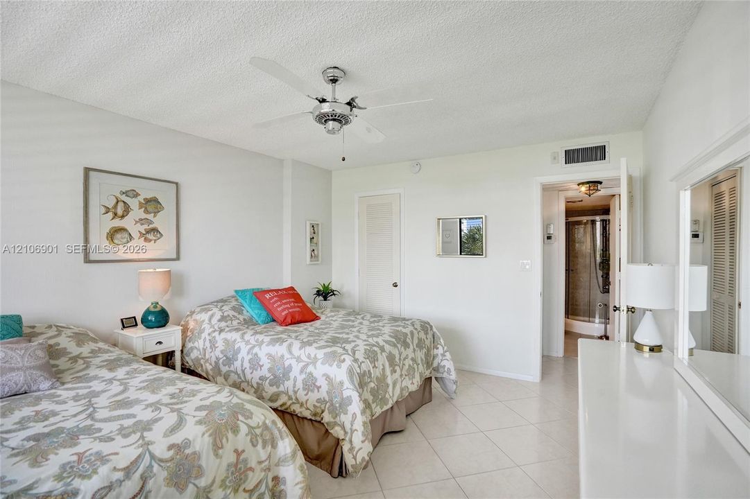 Neutral-toned room featuring large-format tile flooring, a central multi-blade ceiling fan, and a built-in closet with louvered doors
