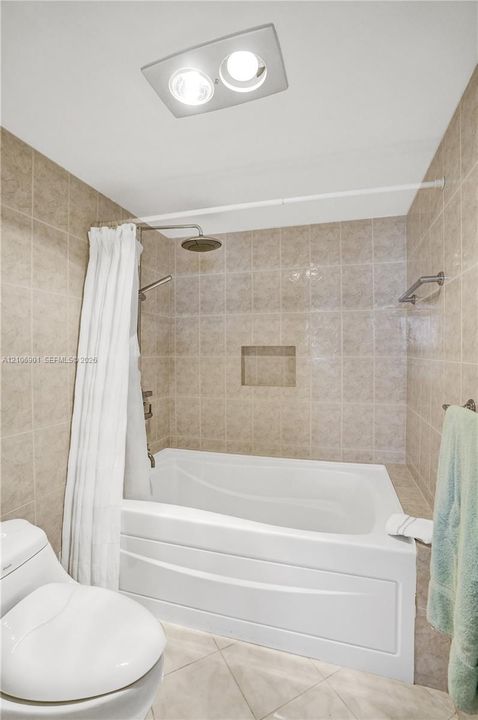 Bathtub with tile surround, built-in recessed wall niche, dual shower head system, and integrated ceiling lighting