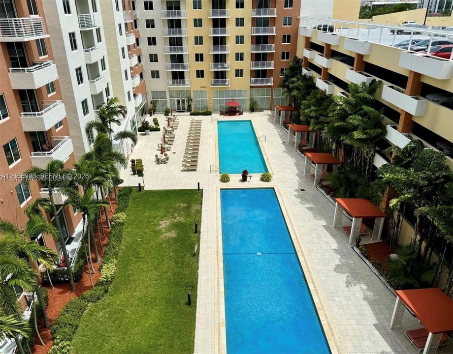 Outdoor amenity area featuring two rectangular swimming pools, stone-paved deck, manicured lawn, and multiple shaded cabanas