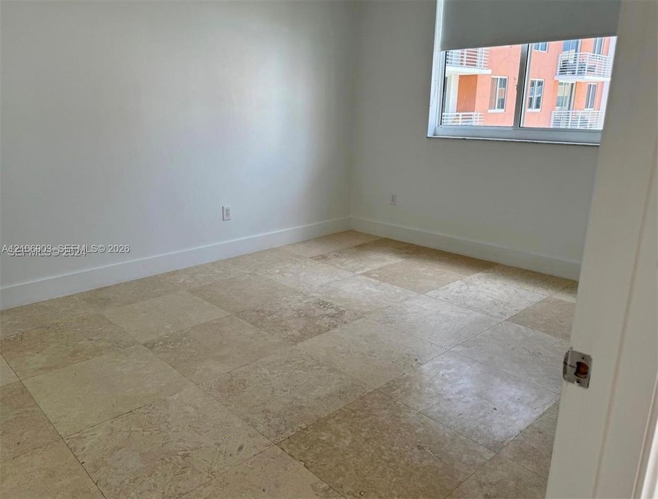 Neutral wall finishes, large-format natural stone tile flooring, and a window with a roller shade