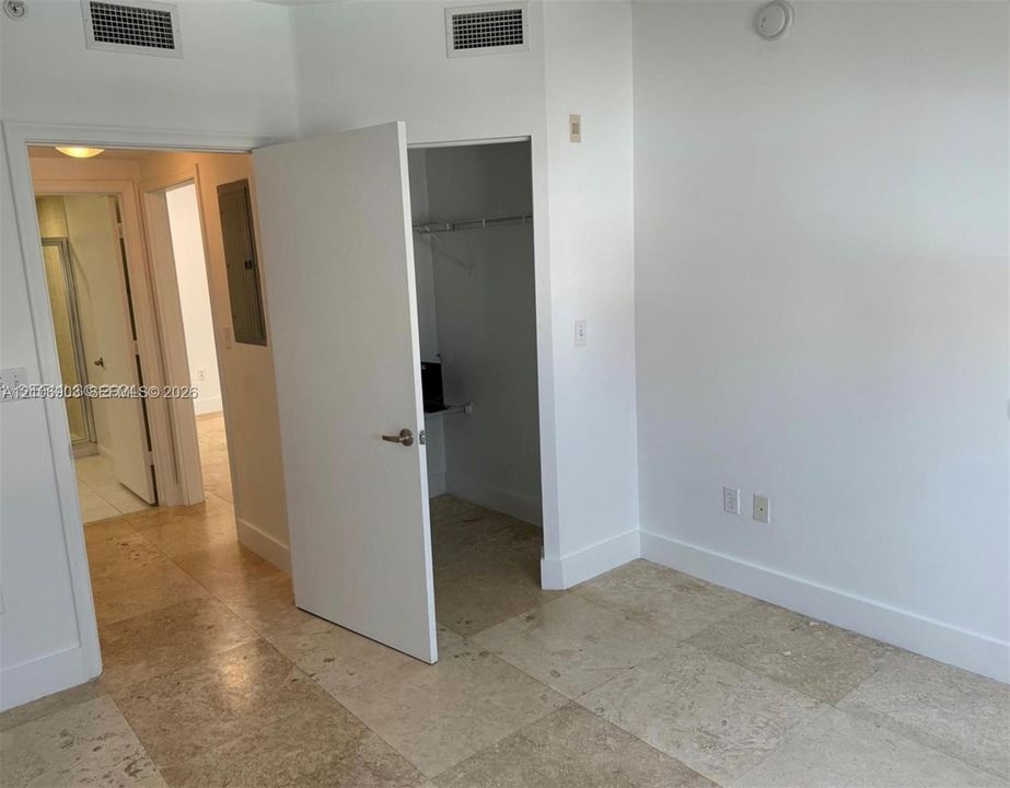 Neutral-toned stone flooring throughout, featuring a walk-in closet with integrated shelving, solid-core interior doors, and overhead lighting fixtures