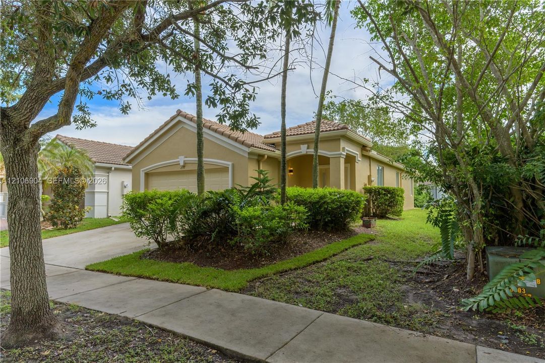 Stucco exterior with a tiled roof, arched entryway, and attached garage, complemented by mature landscaping and a concrete driveway