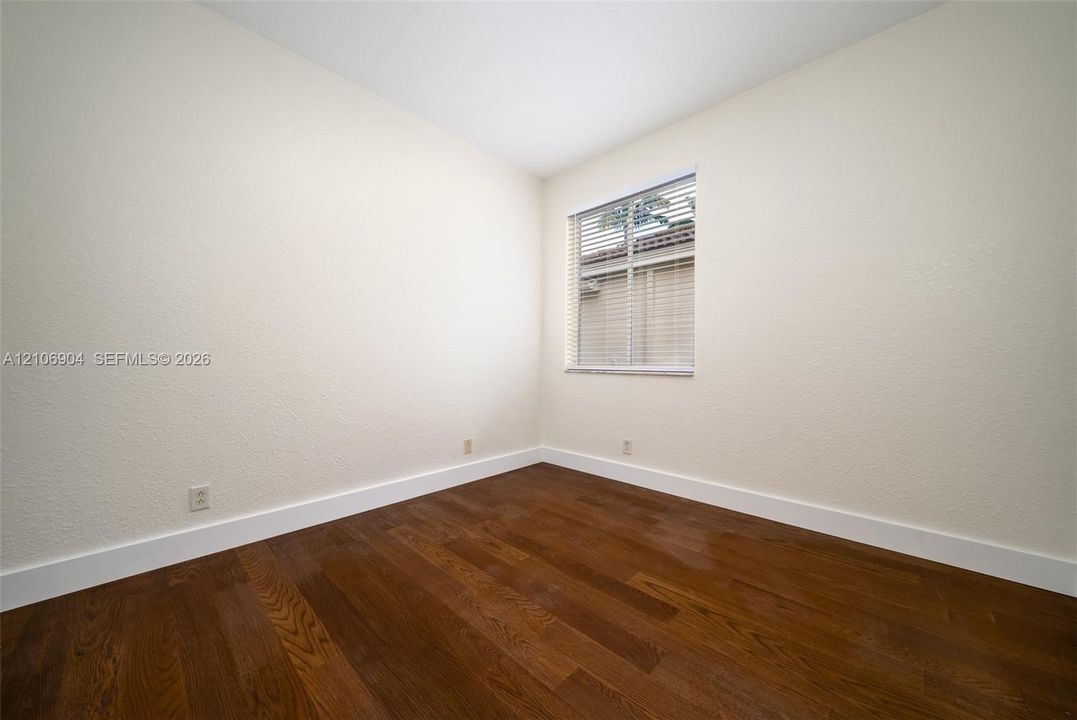 Interior room featuring wood-finish flooring, neutral wall tones, and a window with horizontal blinds