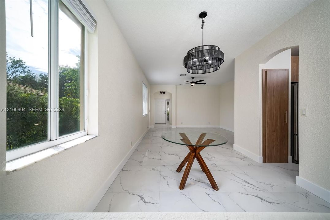 Large-format stone-finish tile flooring, decorative multi-tiered drum chandelier, recessed ceiling lighting, arched entryway, and dual-pane windows