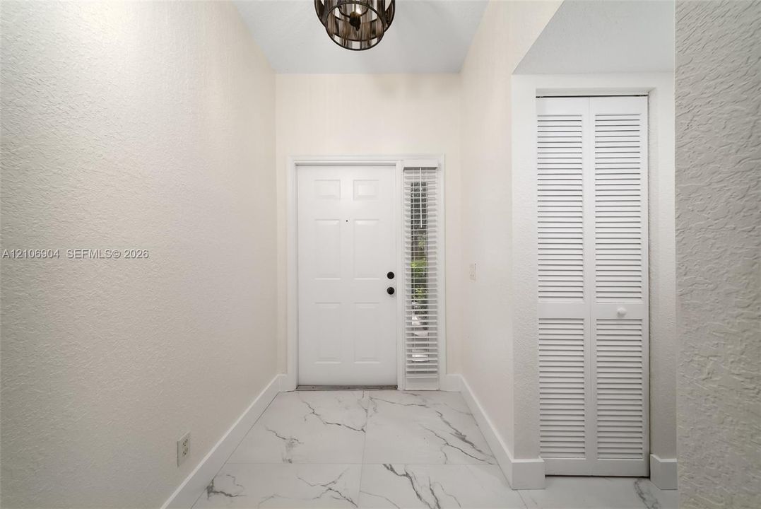 Entryway featuring large-format veined tile flooring, a multi-panel door with a sidelight, a louvered-panel closet door, and a circular drum pendant light fixture