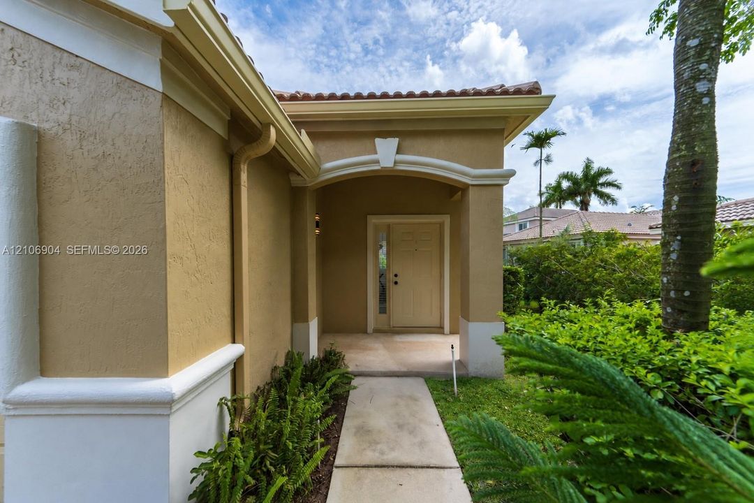 Stucco exterior with an arched covered entryway, a decorative keystone detail, a solid front door with sidelight, and a paved walkway