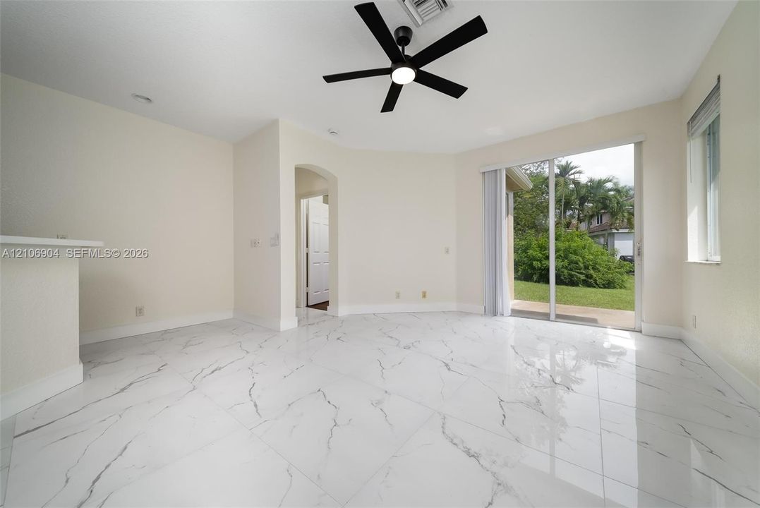 Interior space featuring large-format white tile flooring with dark veining, a matte black ceiling fan with integrated light, an arched entryway, and sliding glass doors