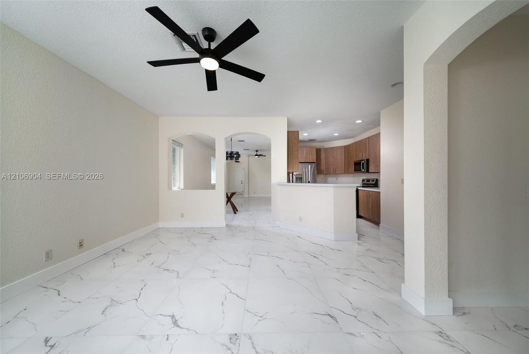 Large-format stone-look tile flooring featuring marbled veining, arched wall openings, neutral wall finish, and modern matte black ceiling fan