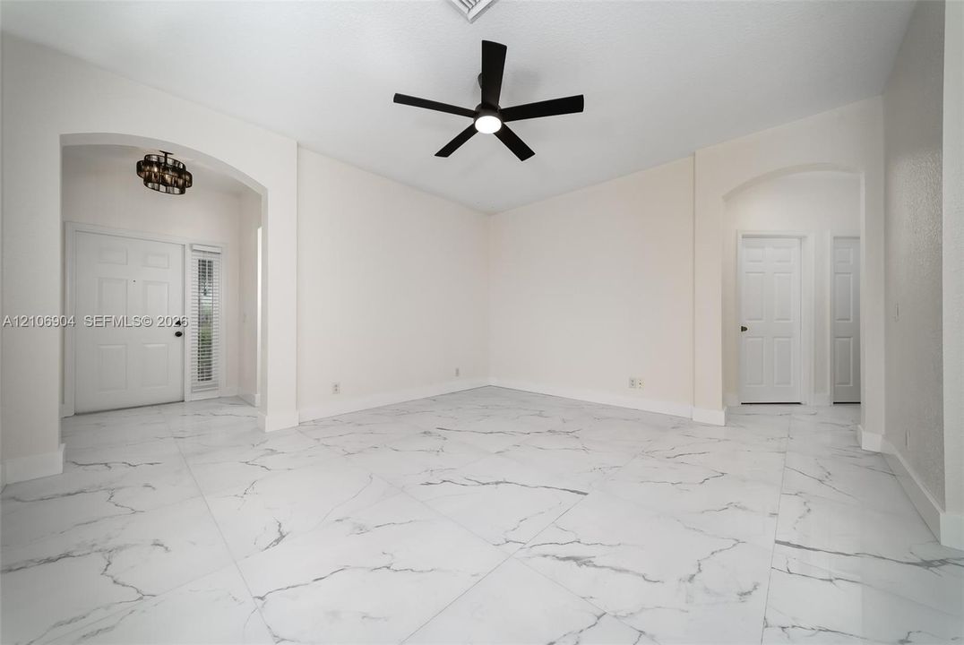 Large-format tile flooring with a neutral-toned veined pattern, recessed archways, matte black ceiling fan with integrated lighting, and multi-panel entry door featuring a vertical glass sidelight